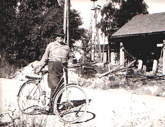 1960 Harjun ukko - Taavetti Kettunen polkupyöränsä kera. Taustalla tuulimoottori, joka nosti taloon talousveden.